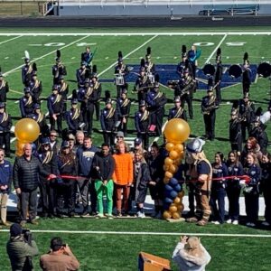 group of people cutting a ribbon on football field filled with marching band